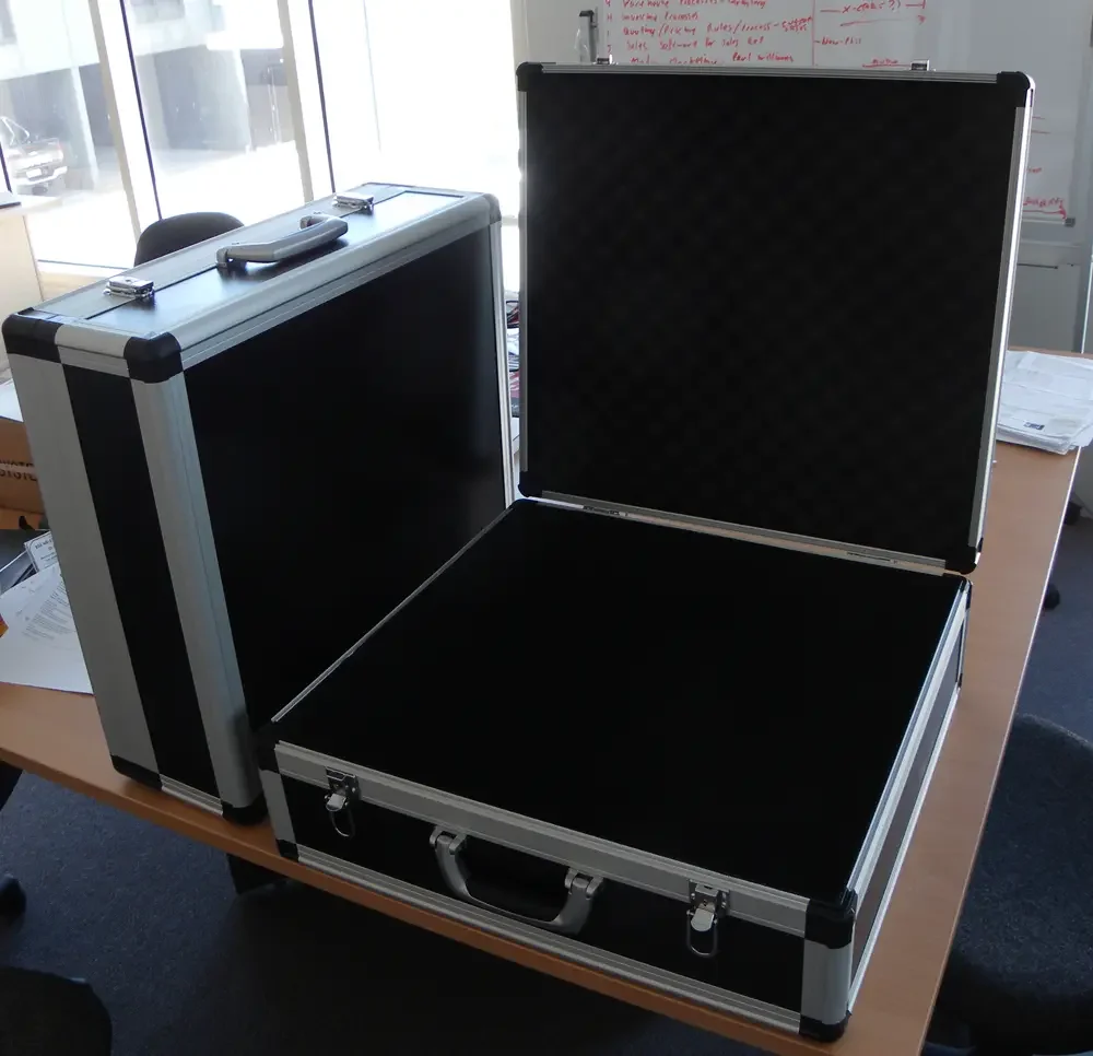 Two black aluminium briefcases on a desk, the open one showing an empty egg-crate foam lid
