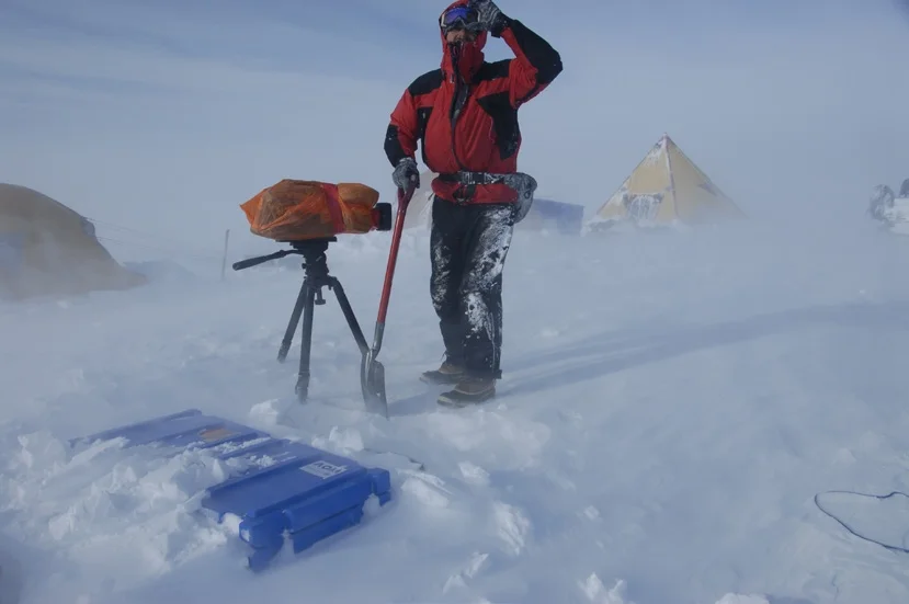 Expedition member digging in a blizzard beside a blue Spacecase half buried in snow