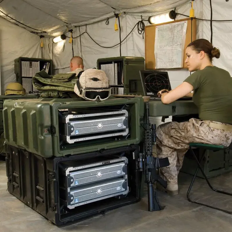 Soldier working a laptop in a field tent beside green rackmount Pelican-Hardigg cases