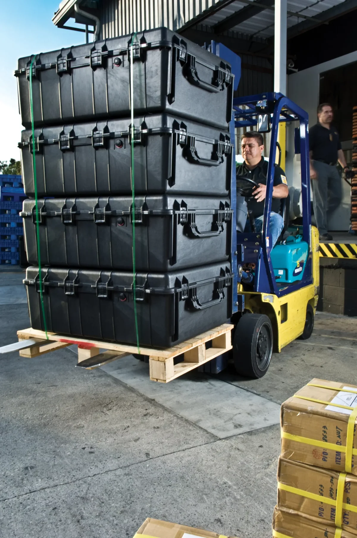 Forklift lifting a strapped pallet of four large black Pelican transit cases