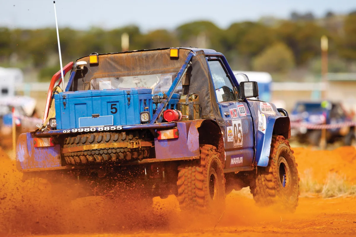 Blue off-road race buggy throwing red dust with a Spacecase mounted behind the cab
