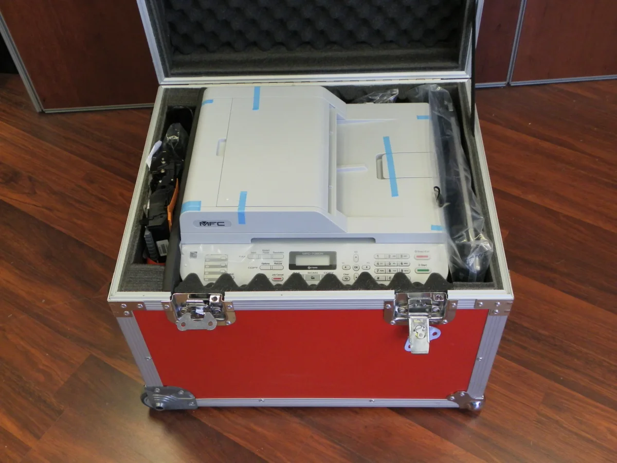 Red flight case holding a multifunction printer in a cut foam cradle