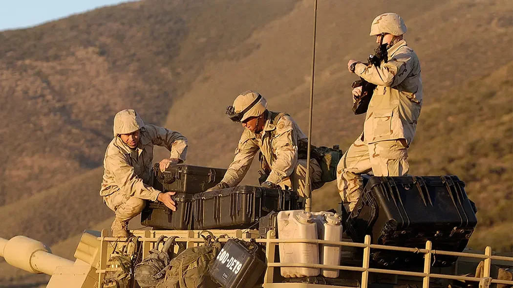 Soldiers loading black Pelican cases onto the deck of an armoured vehicle at dusk