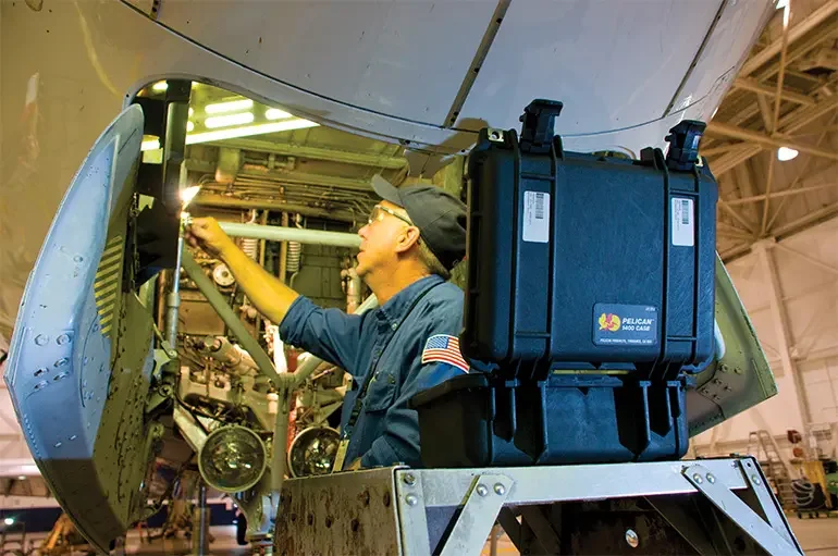 Aircraft technician working under a fuselage with a blue Pelican 1400 case on the platform