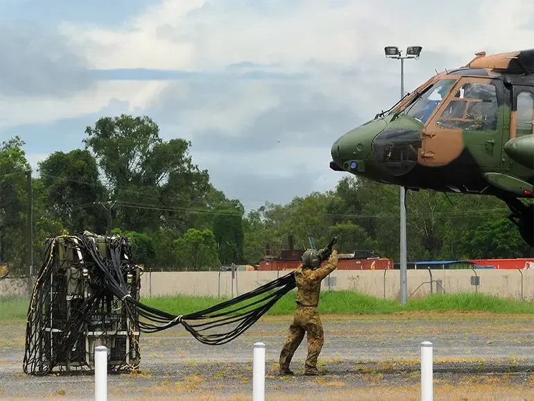 Soldier hooking a cargo net of palletised cases beneath an Australian Army Black Hawk