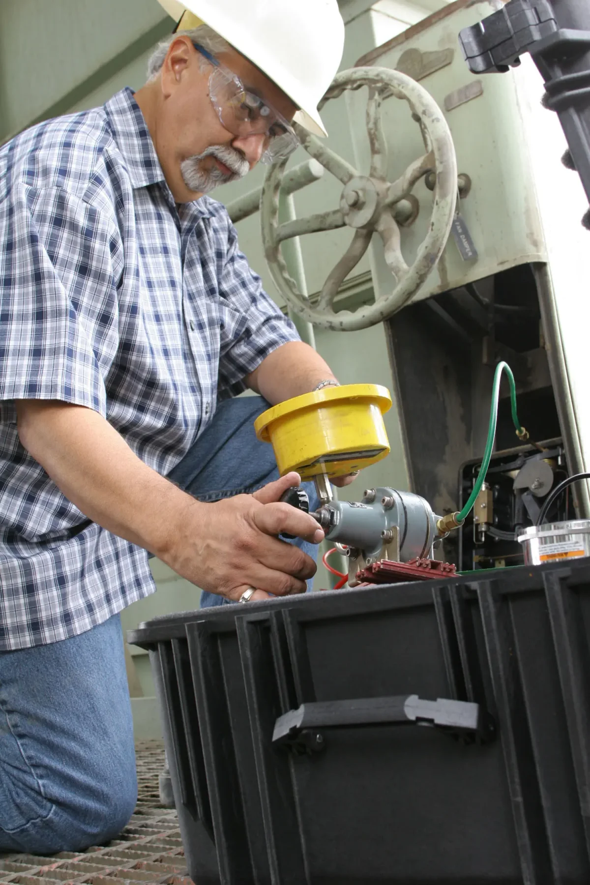 Engineer kneeling at an open black Pelican case while servicing a valve actuator