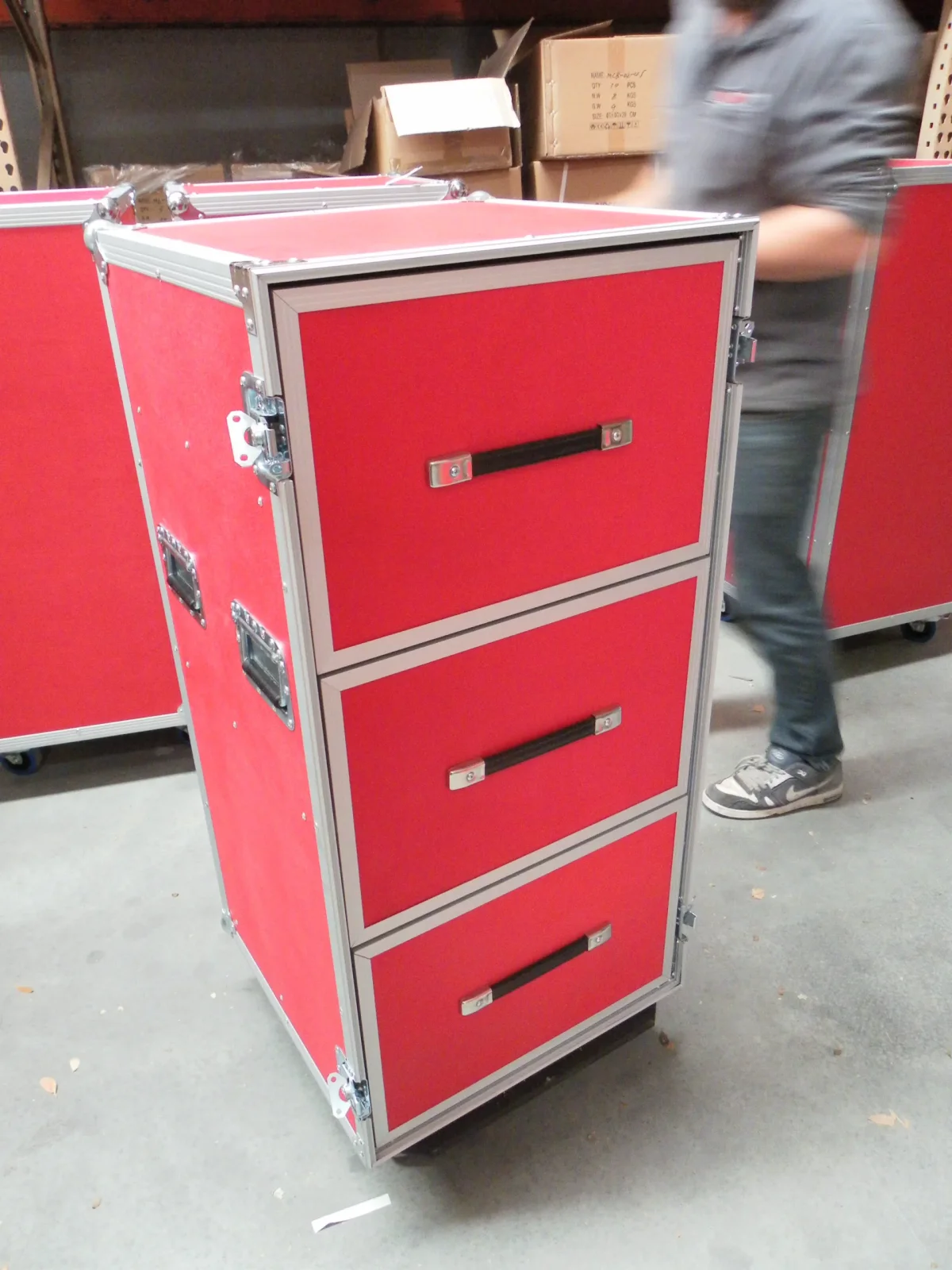 Red three-drawer road case cabinet on castors, a worker moving past