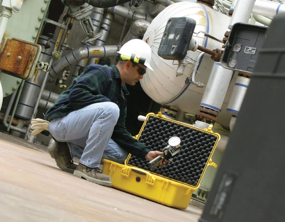 Technician at an open yellow Pelican case with convoluted foam lid, holding a pressure gauge