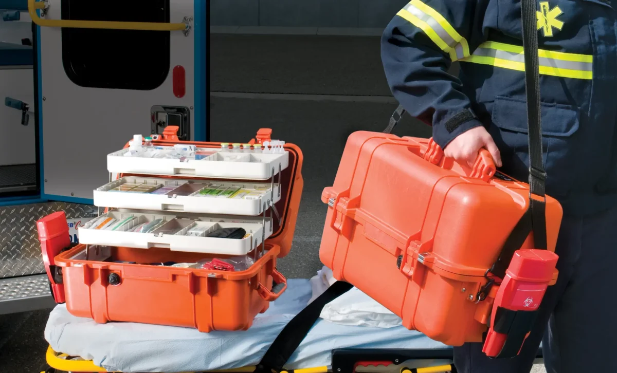 Paramedic carrying an orange Pelican EMS case next to a second case with cantilever trays